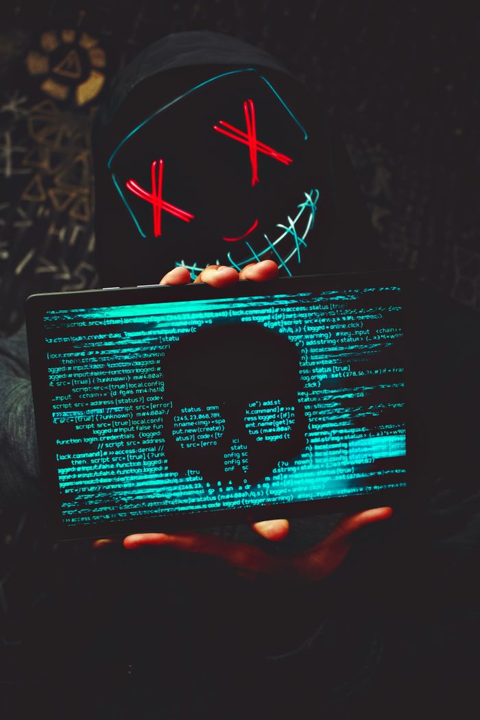 A mysterious person in a neon mask holds a tablet displaying a digital skull.